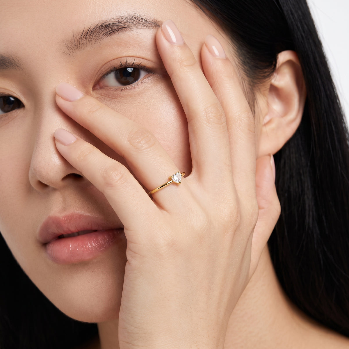 Hand across the face wearing Aimée gold heart ring