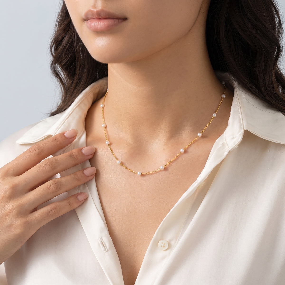 Hand at the collar of a woman wearing the Amalfi Pearl Necklace
