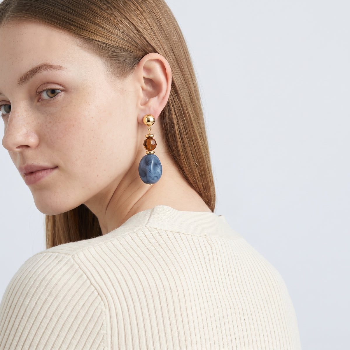 Model wearing the Lelice Amara Blue Marbled Acrylic Statement Drop Earrings in gold, over-the-shoulder glance