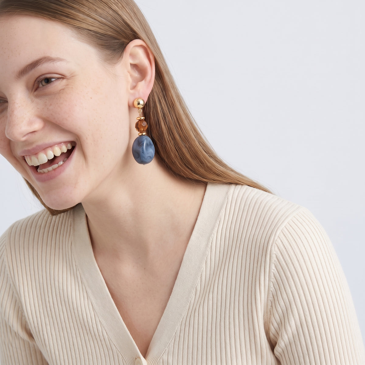 Model wearing the Lelice Amara Blue Marbled Acrylic Statement Drop Earrings in gold, candid laugh