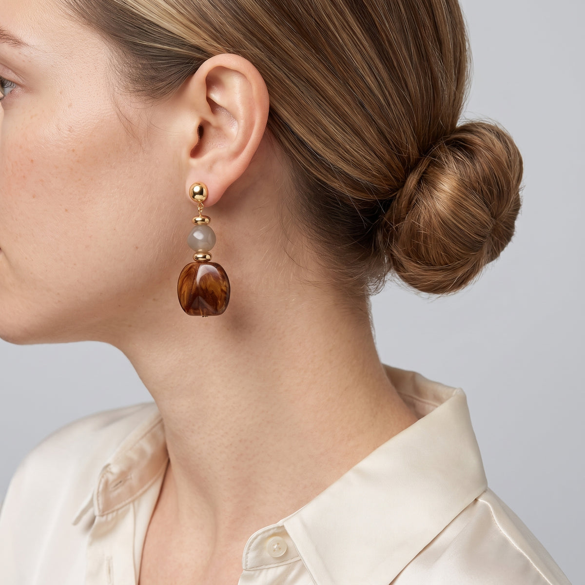 Model wearing the Lelice Amara Brown Marbled Acrylic Statement Drop Earrings in gold, low bun, ear and neck
