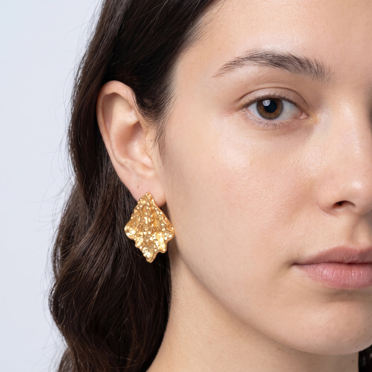 Model wearing the Lelice Artisan Ripple Studs in gold, one-eye face close-up