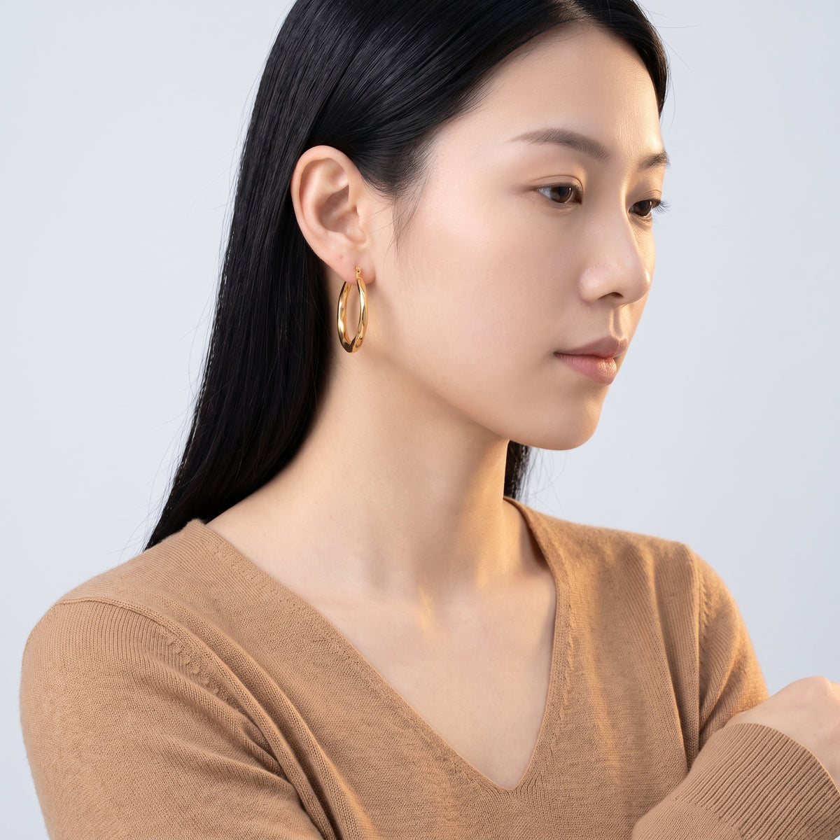 Model wearing the Lelice Claire Polished Hoops in gold, turned toward the light