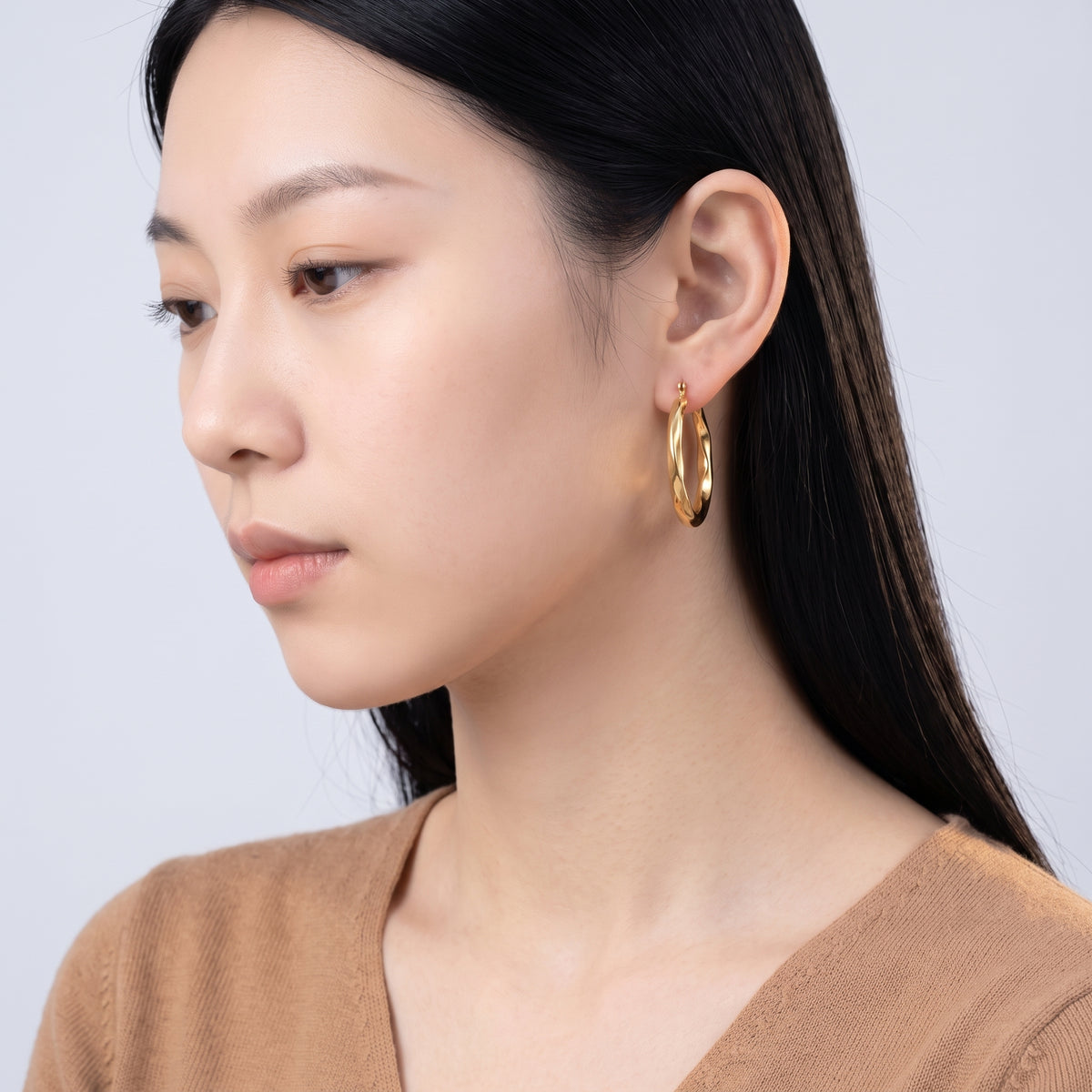 Model wearing the Lelice Claire Polished Hoops in gold, downcast beauty portrait