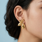 Gold leaf-shaped earring worn by a person with a light blue background