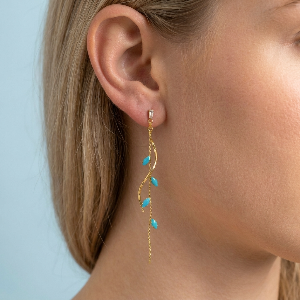 Gold earring with turquoise stones worn by a person against a light blue background