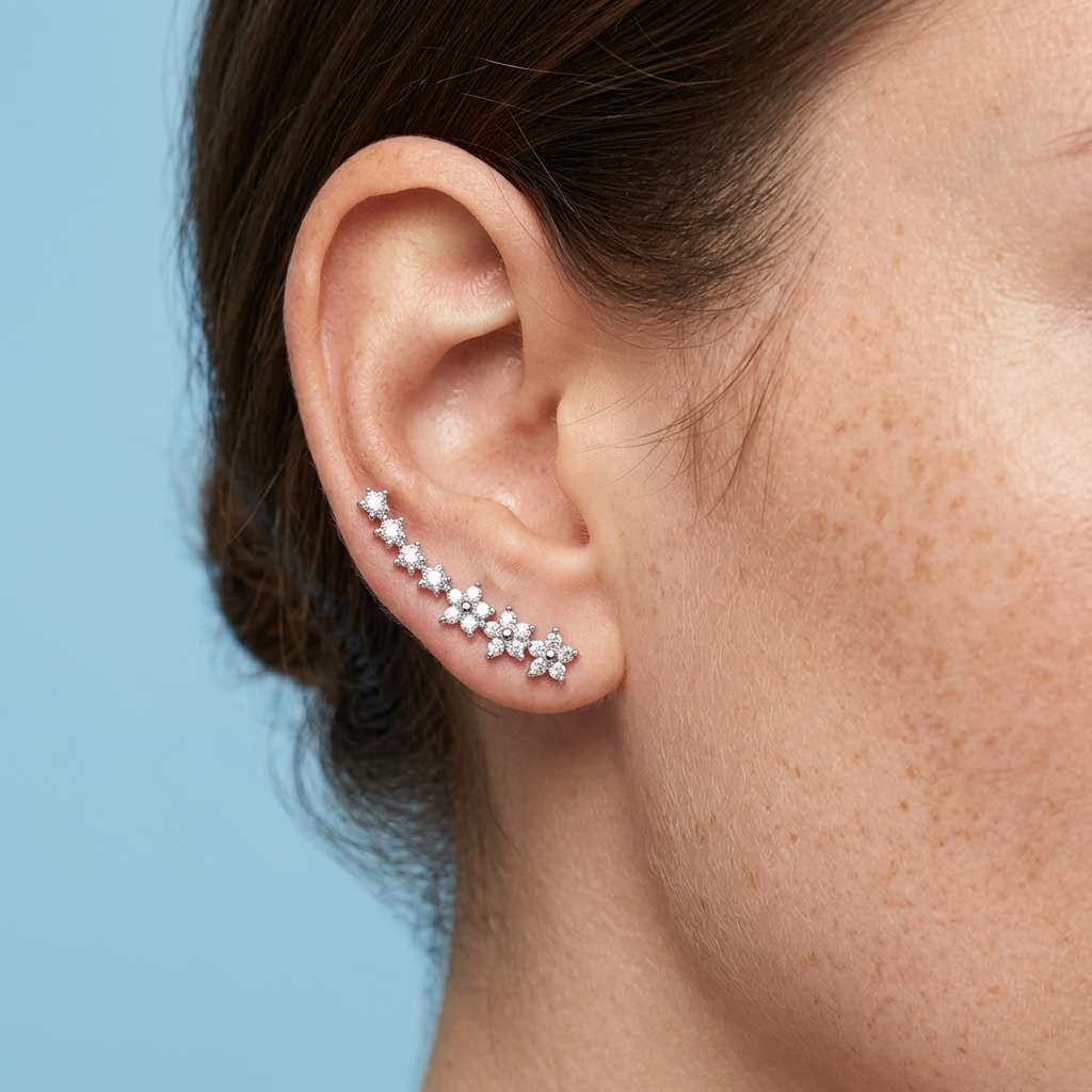 A close-up of a model's ear wearing a curved cluster of silver ear cuffs adorned with small clear stones, set against a solid light blue background.