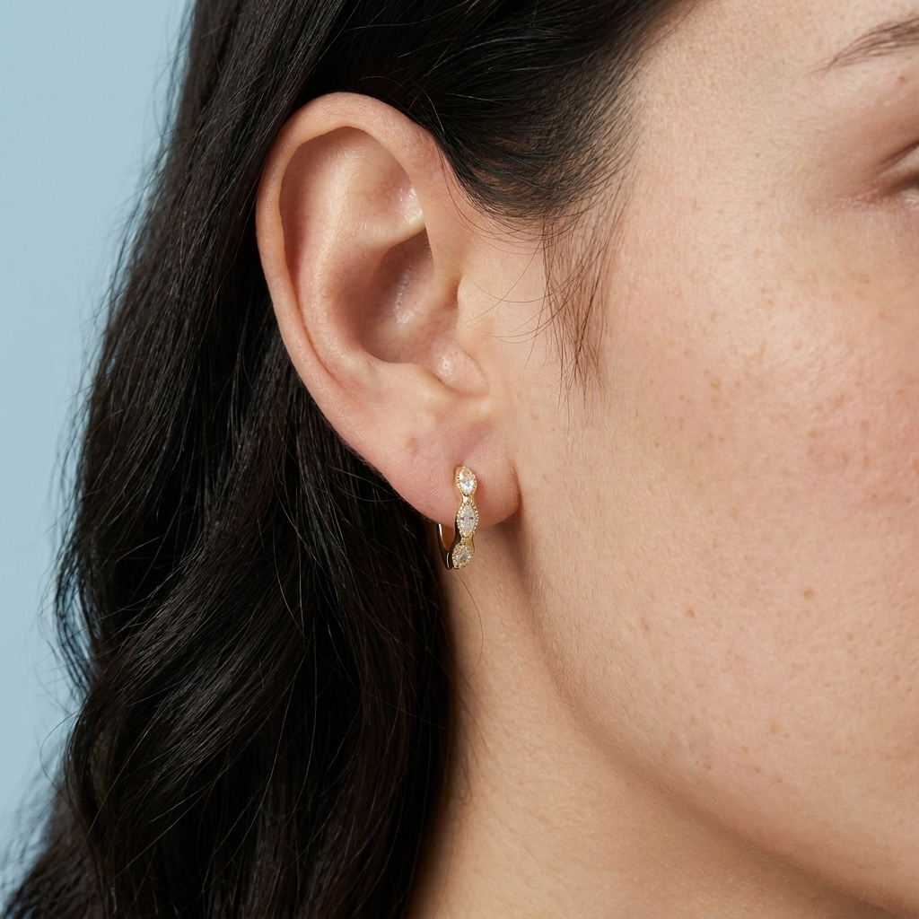Close-up of an ear wearing a gold earring with small stones against a light blue background
