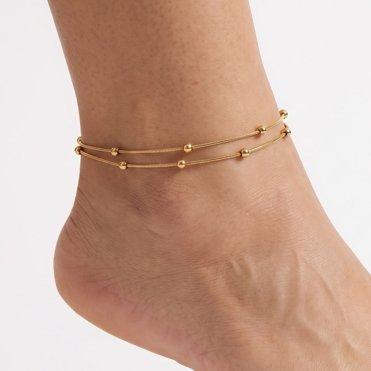 Close-up of the Lelice Elara Double Strand Anklet in gold on a woman's ankle