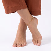 Feet crossed while standing, wearing the Elina Clover Frame Anklet