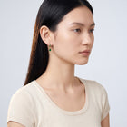Model wearing the Lelice Esme Emerald Hoops in gold, turned toward the light