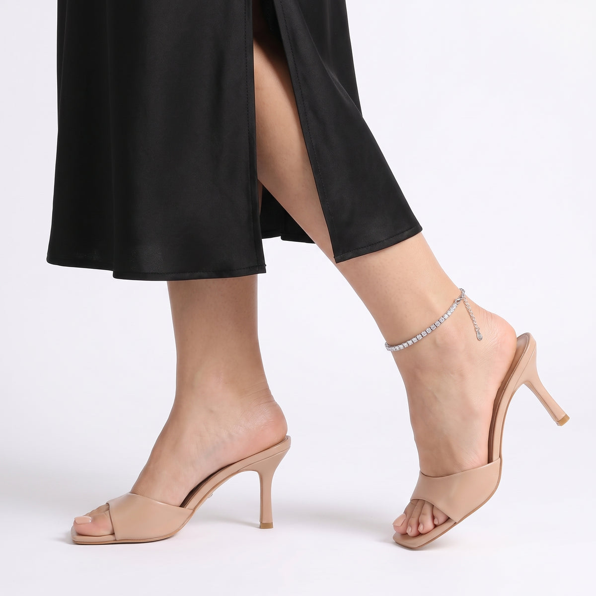 Mid-step in nude heeled mules wearing Eve silver tennis anklet