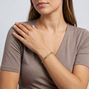 Model wearing the Lelice Armor Gold Bracelet, hand on the opposite shoulder