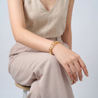 Model wearing the Lelice Miya Gold Clover Bangle, seated, forearm on the knee