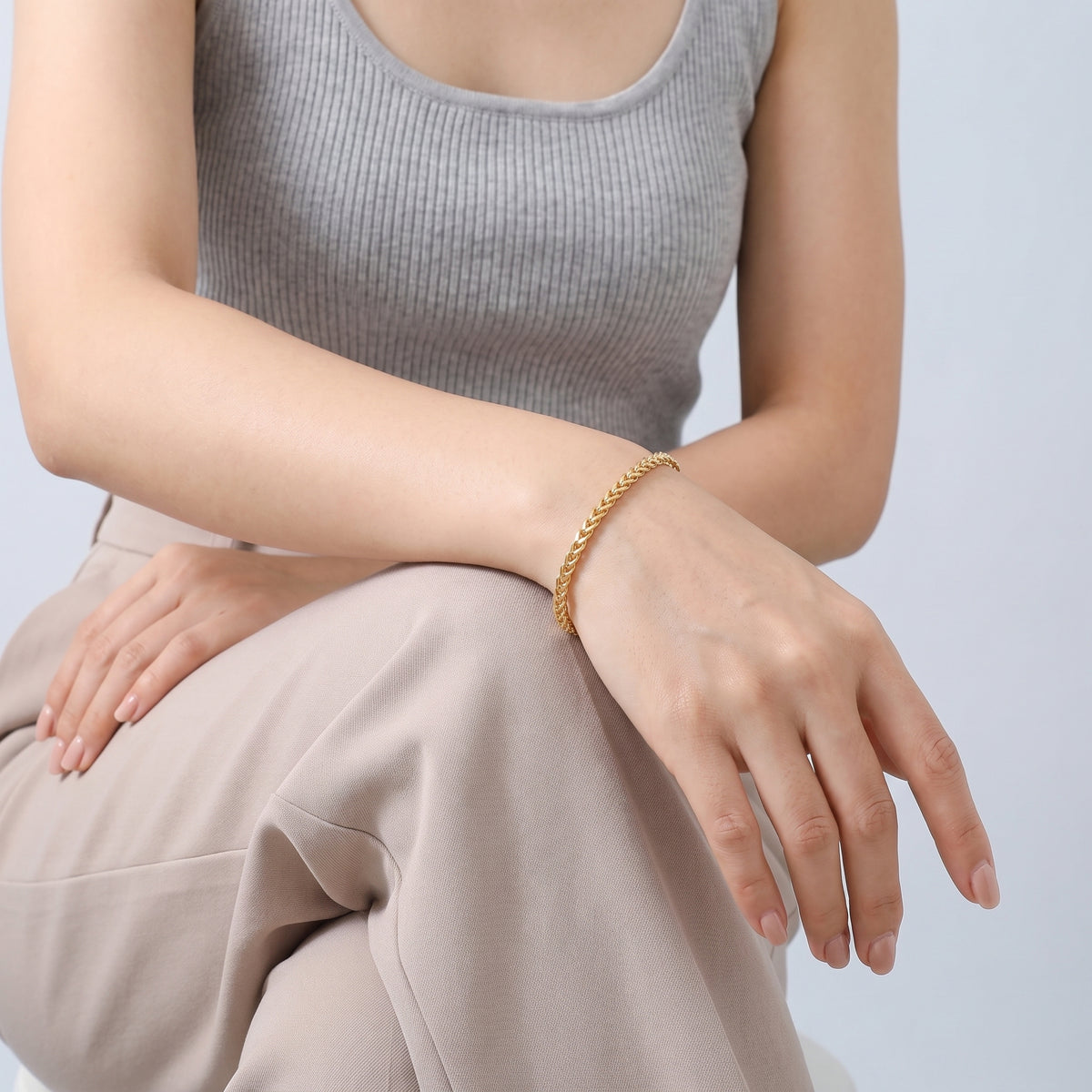 Model wearing the Lelice Monaco Spiga Bracelet in gold, seated, forearm on the knee