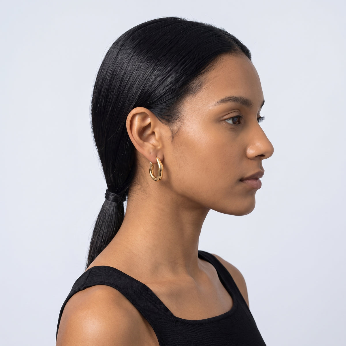 Model wearing the Lelice Maya Hoop Earrings in gold, slicked-back profile
