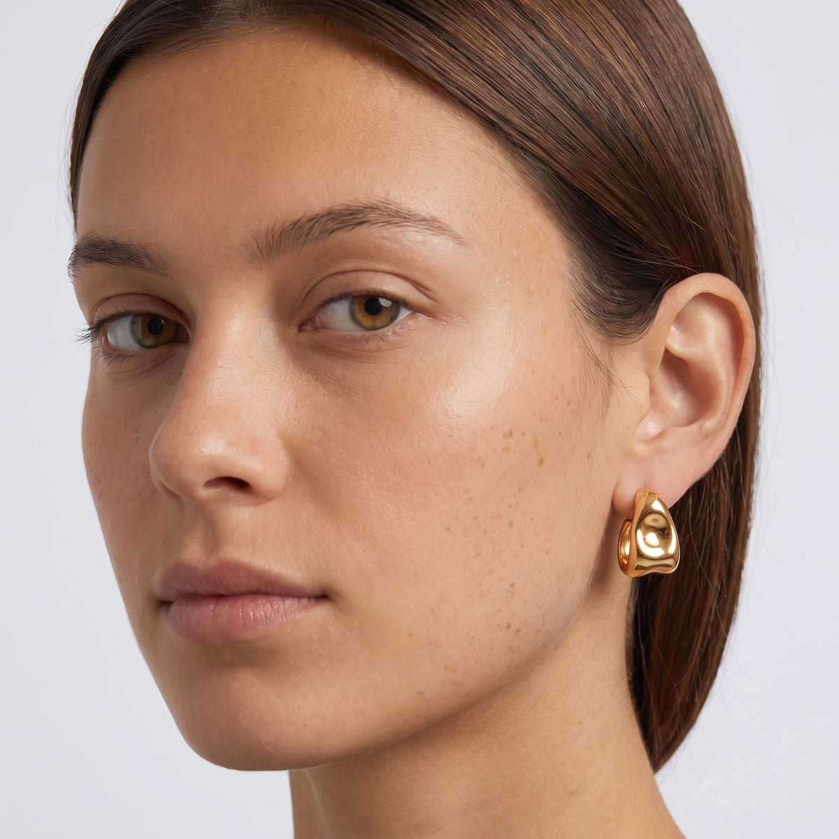 Model wearing the Lelice Maya Ripple Hoops in gold, three-quarter face close-up