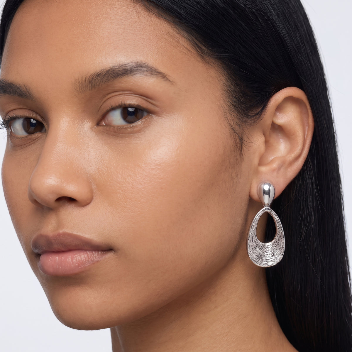 Model wearing the Lelice Nadia Silver Textured Teardrop Statement Earrings, three-quarter face close-up