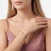 Hand at the neckline wearing Olive gold emerald bracelet