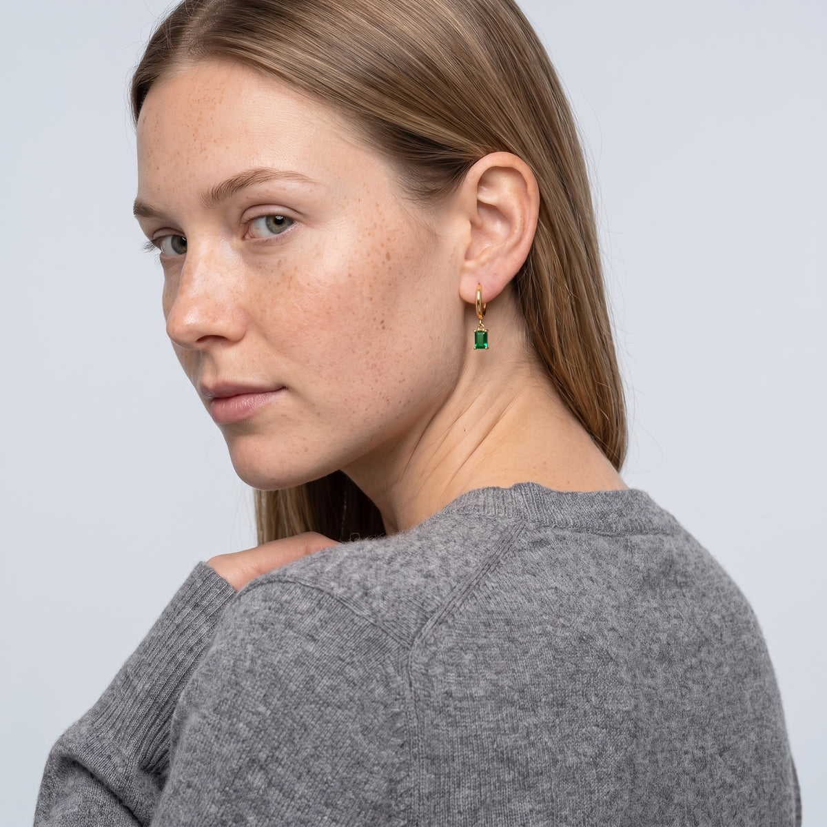 Model wearing the Lelice Piper Emerald Earrings in gold, over-the-shoulder glance