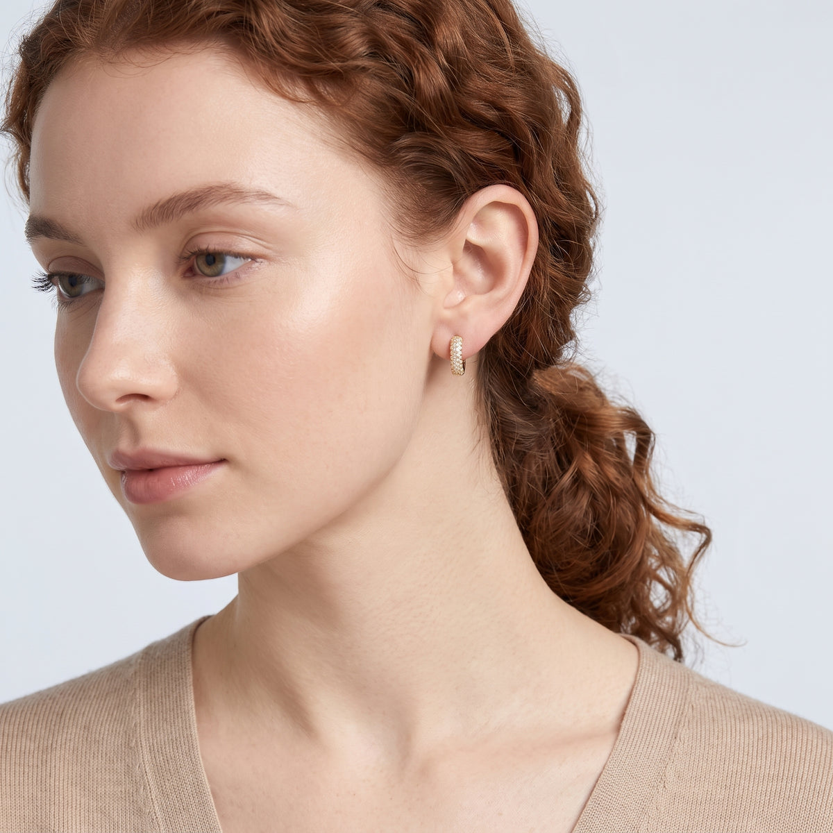 Model wearing the Lelice Remi Huggie Hoops in gold, serene chin lift