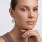 Model wearing the Lelice Sienna Drop Earrings in gold, hand at the chin