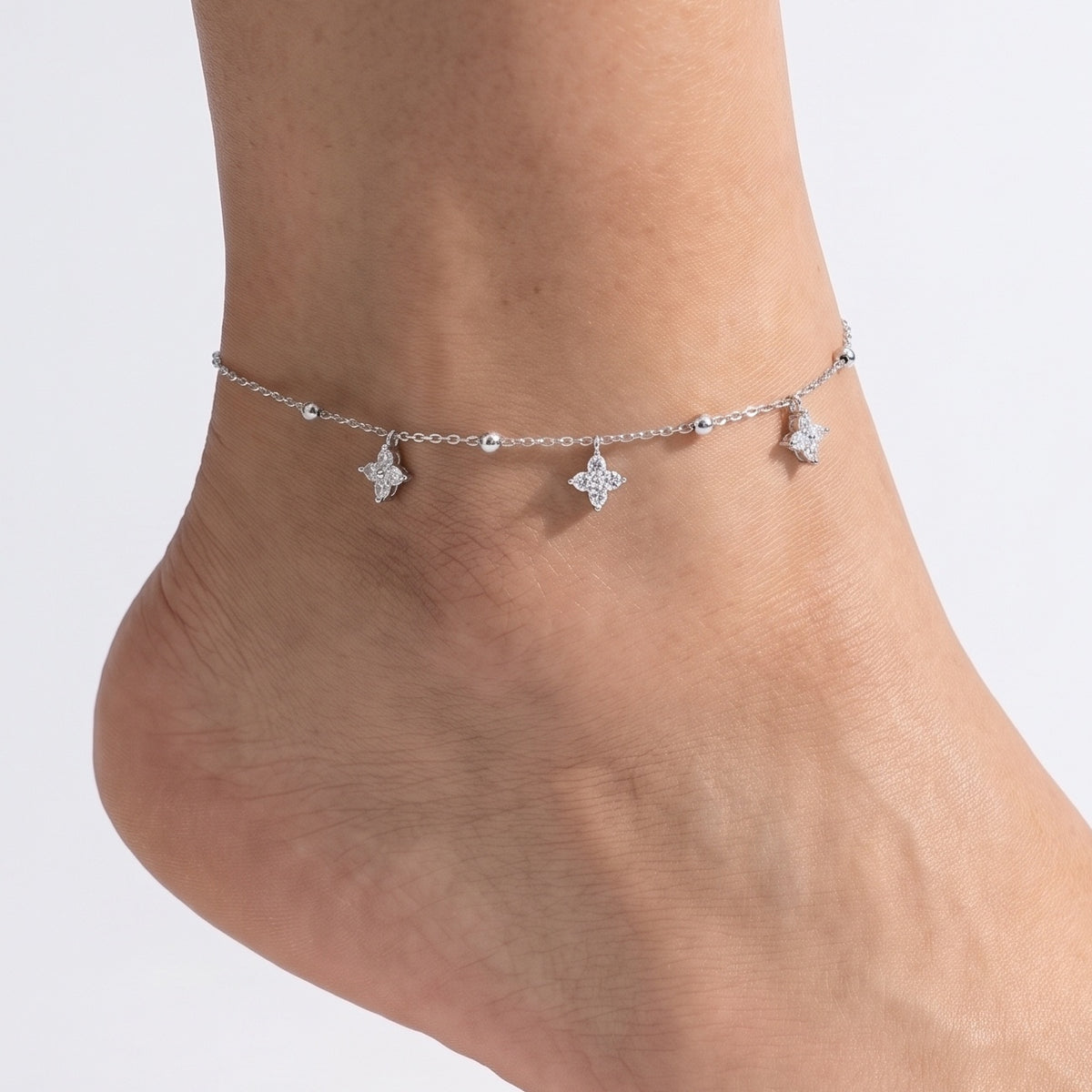 Close-up of the Lelice Silver Clover Charm Anklet on a woman's ankle